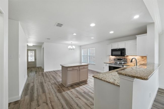 Kitchen with stainless steel electric range, black microwave, light wood finished floors, a kitchen island, and recessed lighting | Image 7