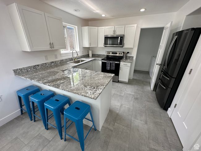 Kitchen featuring stainless steel appliances, a sink, light stone counters, a peninsula, and a kitchen breakfast bar | Image 5