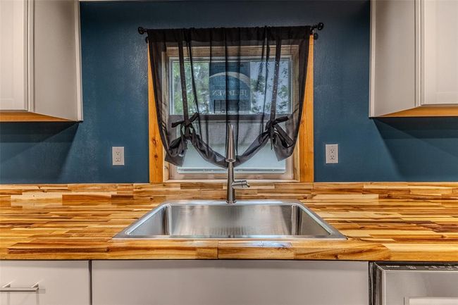 Kitchen view of dishwasher, a sink, white cabinetry, butcher block counters, and tasteful backsplash | Image 12