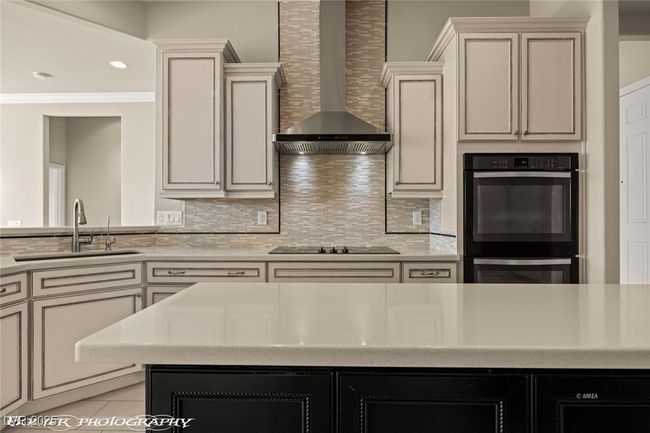 Kitchen with multiple ovens, wall chimney range hood, light countertops, a sink, and black electric stovetop | Image 21