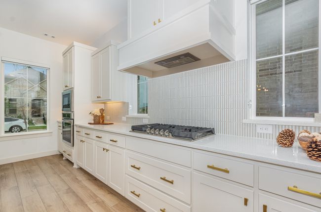 Kitchen with appliances with stainless steel finishes, custom range hood, backsplash, light wood finished floors, and white cabinets | Image 7