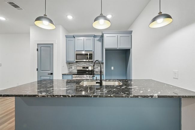Kitchen featuring dark stone counters, visible vents, appliances with stainless steel finishes, a sink, and backsplash | Image 6