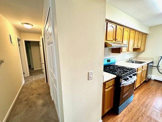Kitchen with appliances with stainless steel finishes, under cabinet range hood, a sink, baseboards, and light countertops | Image 5