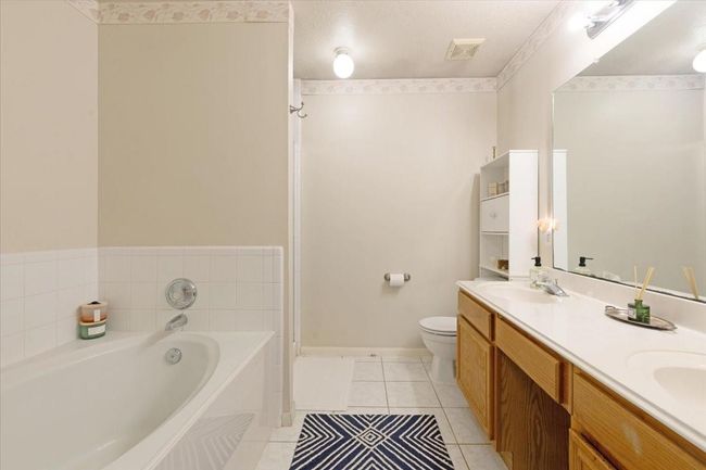 Spacious bathroom with a large bathtub, dual sinks, and ample counter space. Features a neutral color scheme, tile flooring, and a well-lit vanity area. | Image 17