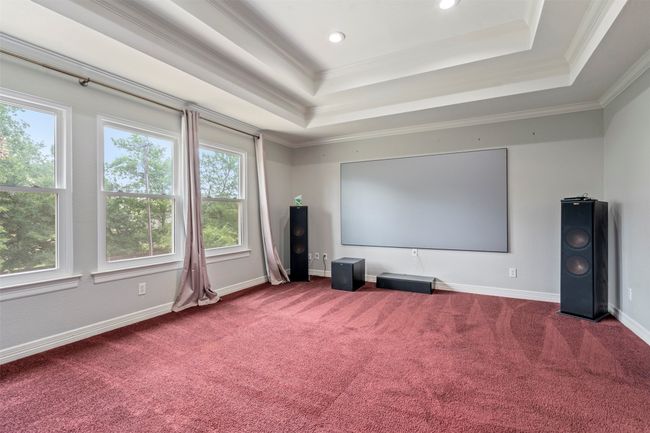 Carpeted home theater room featuring plenty of natural light, a tray ceiling, ornamental molding, baseboards, and recessed lighting | Image 28
