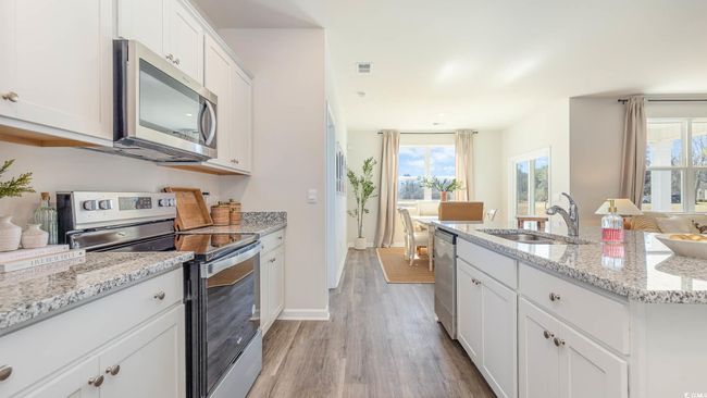 Kitchen featuring white cabinets, appliances with stainless steel finishes, a sink, an island with sink, and light wood-type flooring | Image 5