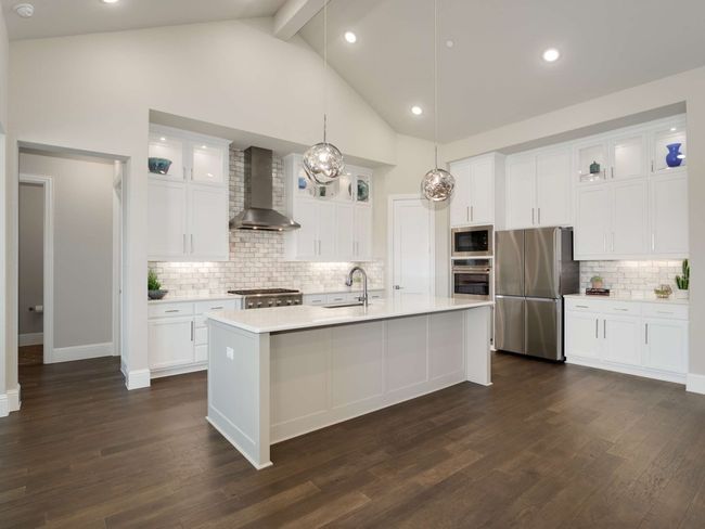 The kitchen is a culinary masterpiece, featuring an expansive island perfect for entertaining, quartz countertops, sleek white cabinetry with glass display fronts, an apron-front farm sink, and high-end stainless-steel appliances, including a six-burner gas cooktop and double convection oven. | Image 4