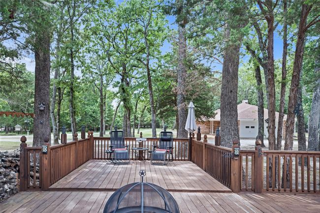 Wooden deck with a fire pit, outdoor dining area, and view of wooded area | Image 29