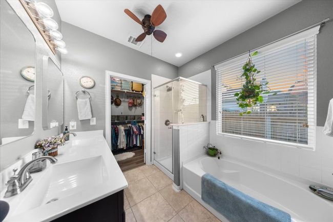 Bathroom featuring a garden tub, a stall shower, double vanity, ceiling fan, and tile patterned flooring | Image 10