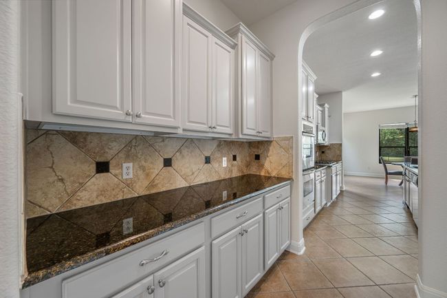 Kitchen featuring tasteful backsplash, arched walkways, recessed lighting, light tile patterned floors, and white cabinets | Image 13