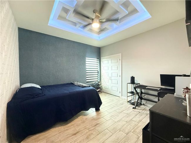 Bedroom with light wood finished floors, an accent wall, a raised ceiling, a ceiling fan, and a desk | Image 11