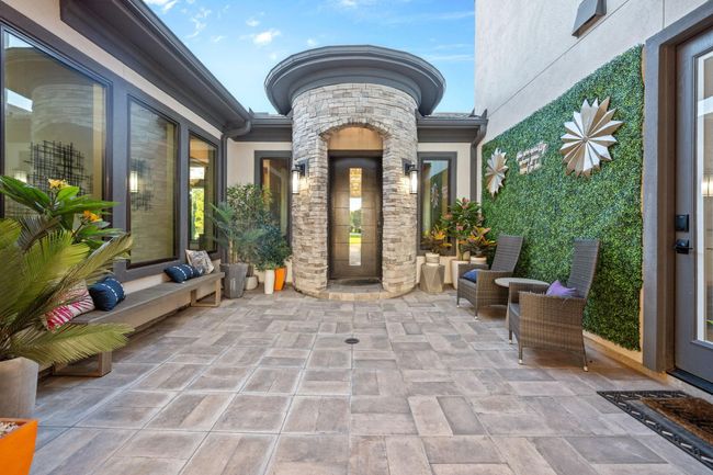 This inviting courtyard features a modern design with elegant stonework and large windows, complemented by lush greenery. Comfortable seating areas and stylish decor create a welcoming outdoor space, perfect for relaxation and entertaining. | Image 4