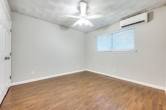 Empty room with a wall mounted air conditioner, a ceiling fan, and wood finished floors | Image 7