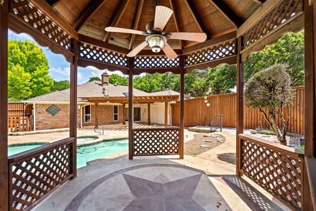 Fenced backyard featuring a gazebo, an in-ground hot tub, a ceiling fan, and a patio | Image 11