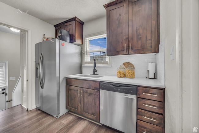 Kitchen with appliances with stainless steel finishes, a sink, wood finished floors, backsplash, and light countertops | Image 8