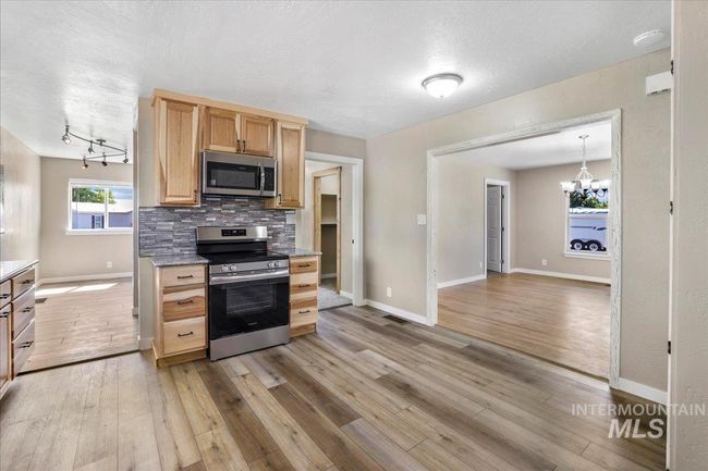 Kitchen with appliances with stainless steel finishes, light brown cabinets, decorative backsplash, light wood finished floors, and a textured ceiling | Image 21