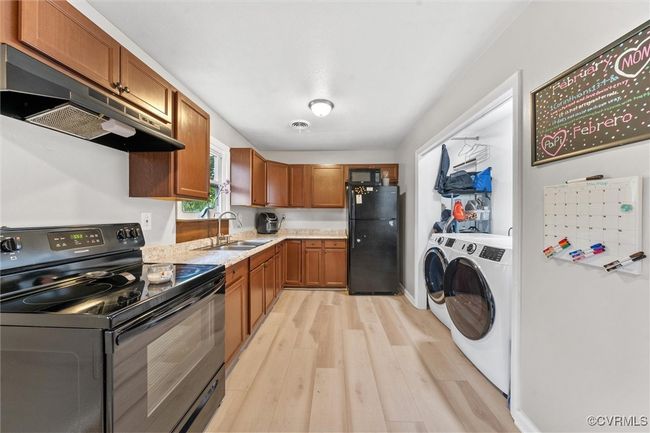 Kitchen with a sink, light wood-style floors, under cabinet range hood, black appliances, and separate washer and dryer | Image 17
