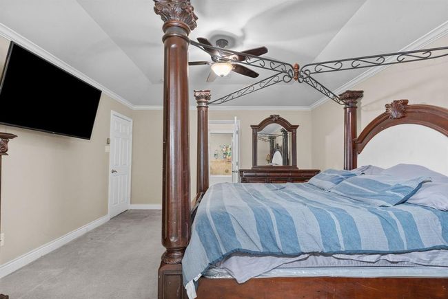 This is a well-maintained bedroom featuring a large four-poster bed, neutral walls, ceiling fan, and wall-mounted TV. It has carpeted flooring and includes a dresser with a mirror. | Image 45