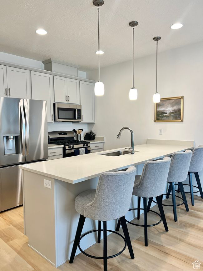 Kitchen featuring stainless steel appliances, a breakfast bar area, a peninsula, light wood-style flooring, and pendant lighting | Image 4