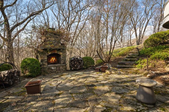 Tucked among the trees, a charming stone patio with a wood-burning fireplace offers a cozy and private setting for gathering year-round. | Image 43