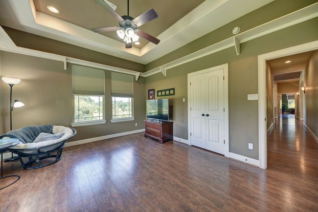 2nd Picture of Flex room (bedroom, media/game room, or craft/hobby room) features a tray ceiling with recessed lighting, and a ceiling fan. Large windows provide ample natural light. The room connects to a hallway leading to other parts of the house, creating an open and inviting atmosphere. | Image 26