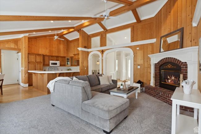 Living room featuring a ceiling fan, wooden walls, light carpet, a fireplace, and arched walkways | Image 6