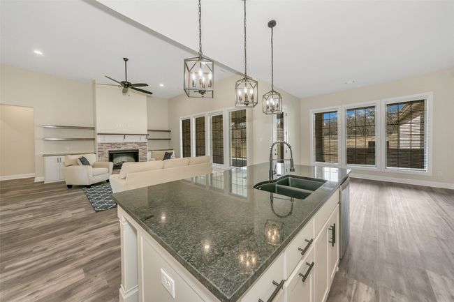 Kitchen featuring ceiling fan with notable chandelier, a fireplace, wood finished floors, and a sink | Image 8