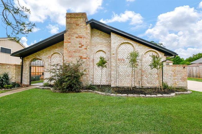 This charming home features a unique brick exterior with arched accents and a prominent chimney. A well-maintained lawn and tasteful landscaping enhance its curb appeal, while a gated entrance adds a touch of elegance and security. | Image 7