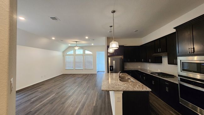 Kitchen with stainless steel appliances, a sink, tasteful backsplash, light stone countertops, and dark wood-style flooring | Image 6