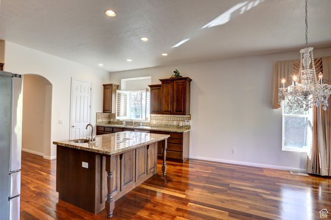 Kitchen with arched walkways, a sink, dark wood-style flooring, freestanding refrigerator, and a center island with sink | Image 17