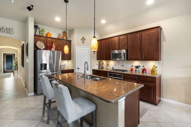 Kitchen with stainless steel appliances, a sink, light tile patterned floors, decorative backsplash, and a center island with sink | Image 10
