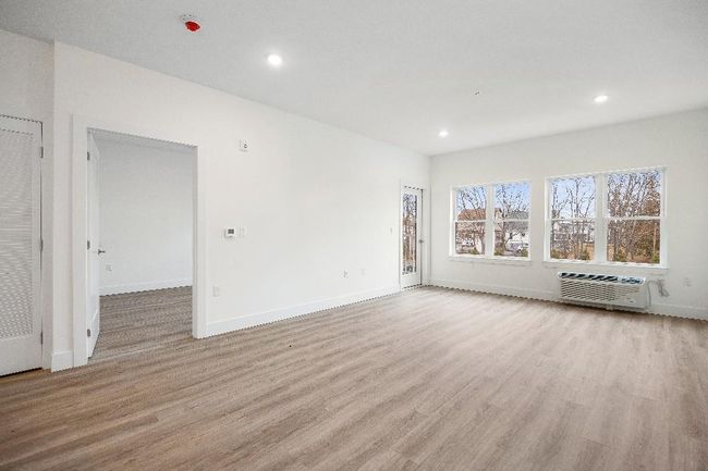 Unfurnished living room featuring an AC wall unit, light wood-style floors, recessed lighting, and baseboards | Image 36