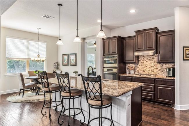 Kitchen with tasteful backsplash, a chandelier, a kitchen breakfast bar, light stone counters, and dark brown cabinetry | Image 7