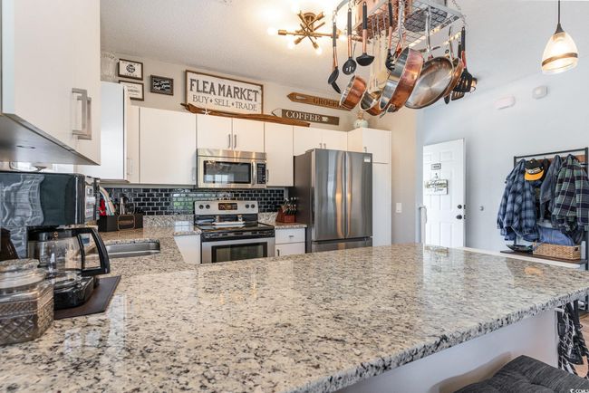 Kitchen featuring tasteful backsplash, white cabinetry, stainless steel appliances, a peninsula, and light stone countertops | Image 7