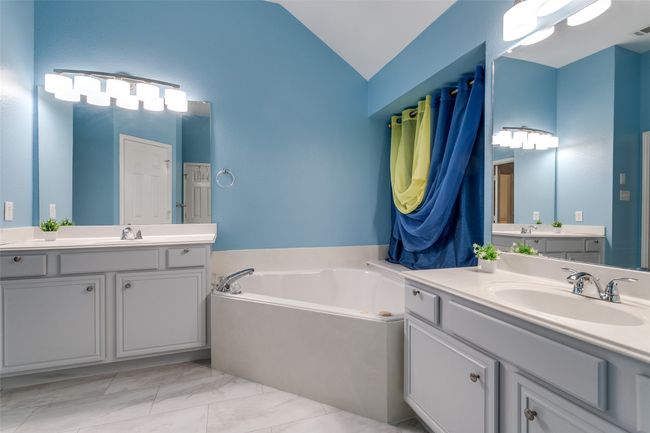 Full bathroom featuring lofted ceiling, two vanities, a bath, and marble finish flooring | Image 15