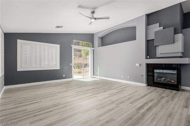 Great room with ceiling fan, a glass covered fireplace, wood finished floors, and vaulted ceiling | Image 6