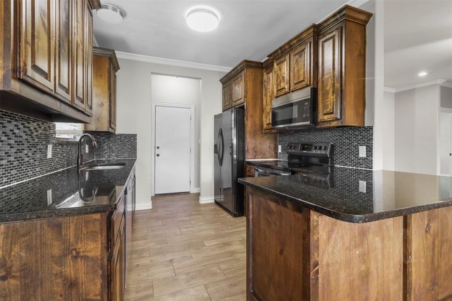 Kitchen with black appliances, backsplash, crown molding, a peninsula, and dark stone counters | Image 6