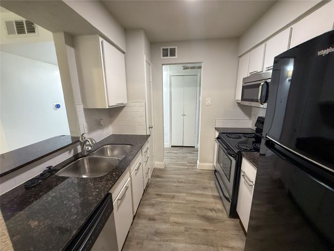Kitchen with stainless steel appliances, white cabinets, light wood-style floors, dark stone counters, and tasteful backsplash | Image 16