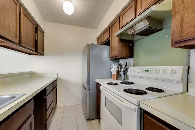 Kitchen with electric range, sink, light tile patterned flooring, and a textured ceiling | Image 6
