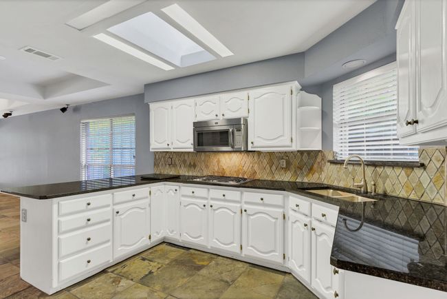 Kitchen with stainless steel appliances, a peninsula, a skylight, white cabinetry, and backsplash | Image 14