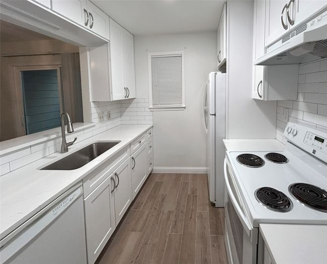 Kitchen with white appliances, white cabinets, backsplash, and stainless-steel sink | Image 13