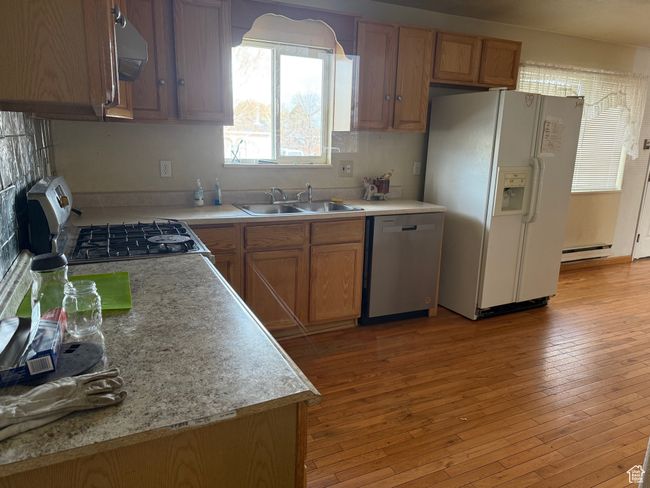 Kitchen with a baseboard heating unit, a sink, white refrigerator with ice dispenser, gas stove, and dishwasher | Image 8