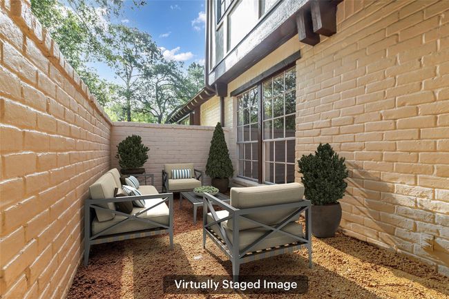 This virtually staged photo showcases a cozy, enclosed patio area with brick walls. It is virtually staged with comfortable seating and potted plants. | Image 5