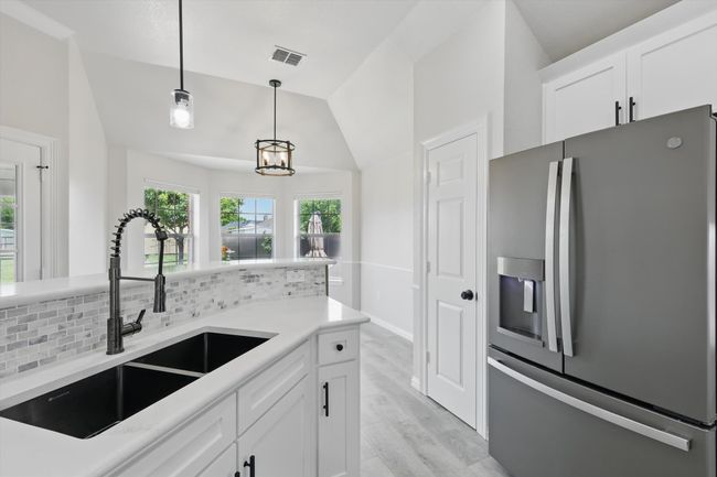 Kitchen featuring stainless steel fridge, a sink, vaulted ceiling, hanging light fixtures, and white cabinets | Image 15