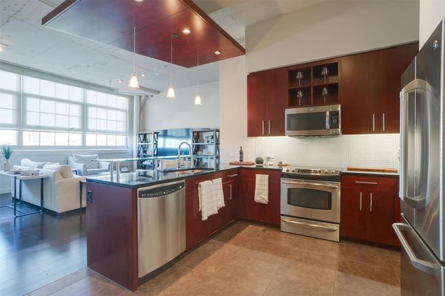 Kitchen featuring appliances with stainless steel finishes, dark countertops, tasteful backsplash, a peninsula, and decorative light fixtures | Image 11
