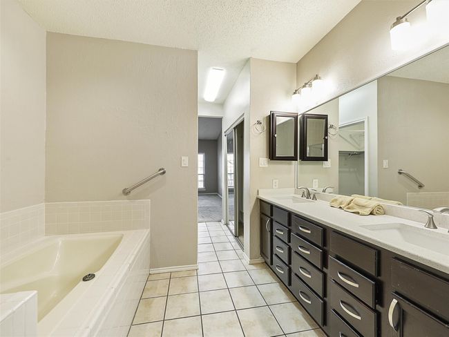 Full bathroom with double vanity, a sink, tile patterned flooring, a textured ceiling, and a bath | Image 16
