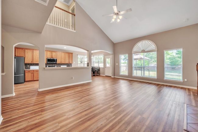 Unfurnished living room featuring light wood-style flooring, arched walkways, baseboards, a ceiling fan, and high vaulted ceiling | Image 14