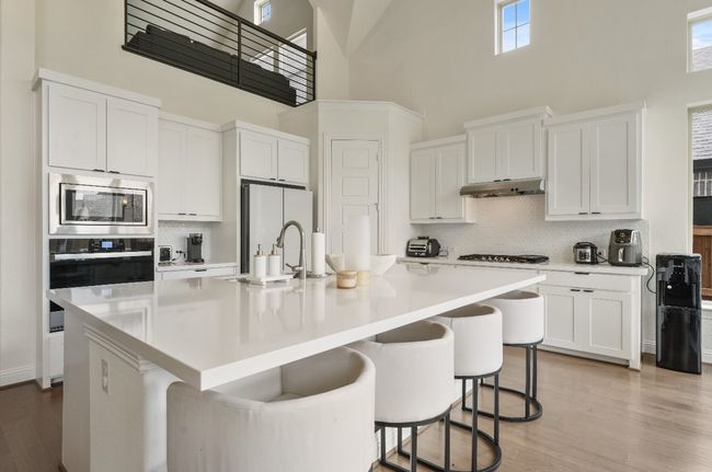 Kitchen with appliances with stainless steel finishes, a towering ceiling, a sink, backsplash, and light wood-style flooring | Image 5