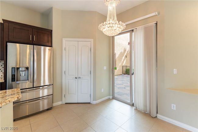 Kitchen with stainless steel fridge, an inviting chandelier, pendant lighting, light stone countertops, and dark brown cabinetry | Image 11