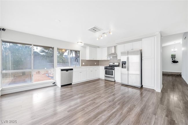Kitchen with wall chimney range hood, tasteful backsplash, white cabinets, a sink, and appliances with stainless steel finishes | Image 5
